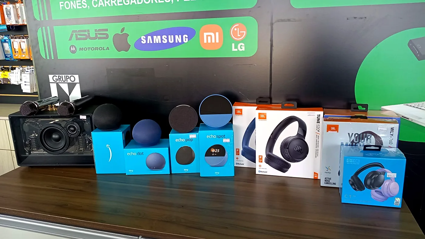Caixa de som com microfones, Amazon Echo Dot, Echo Pop, Echo Spot e headphones JBL expostos no balcão