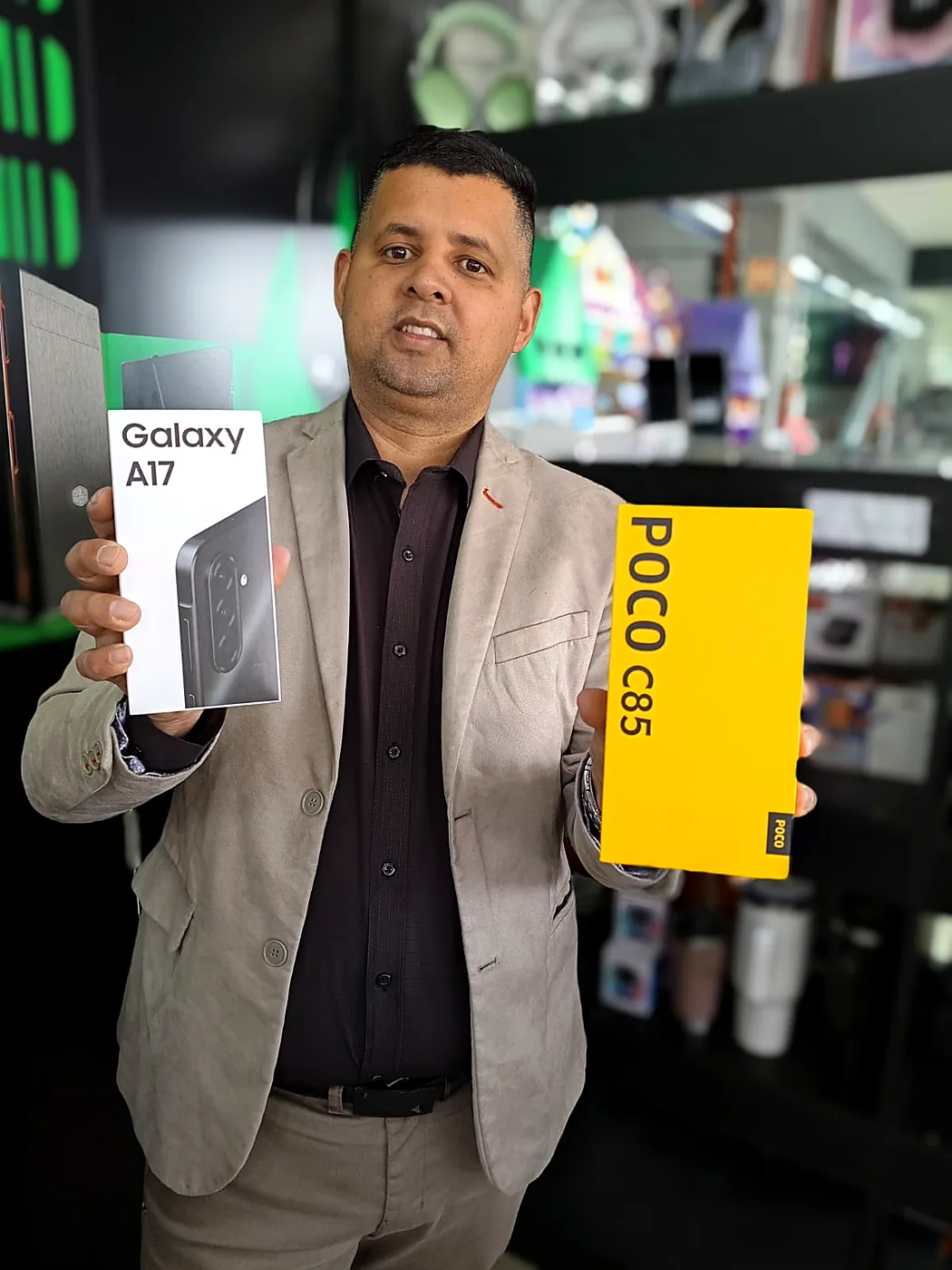 Junior Rosa Caria, CEO da Infotech, dentro da loja segurando as caixas de um Samsung Galaxy A17 e de um Xiaomi POCO C85