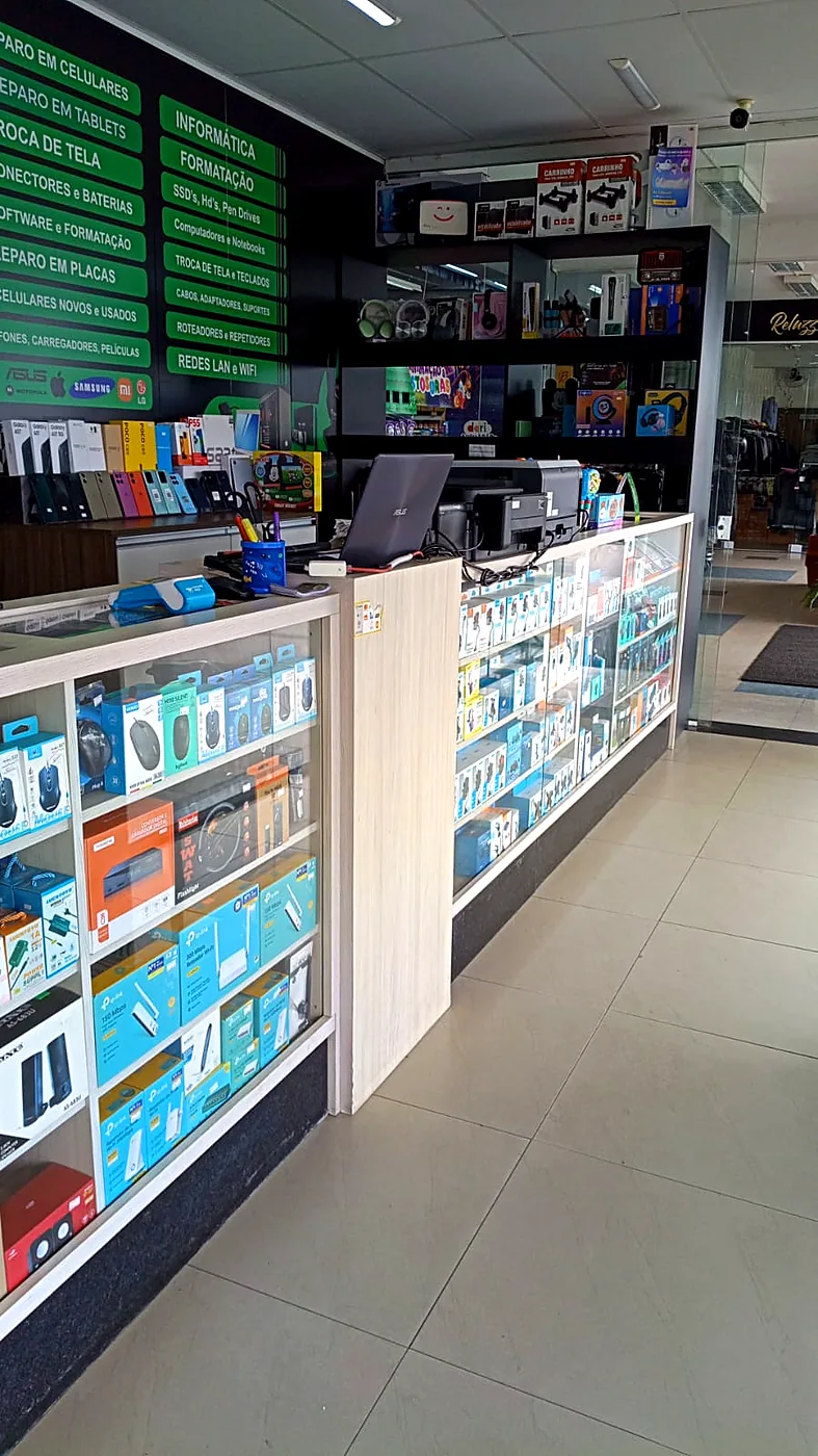 Painel verde de serviços na parede da Infotech, com faixas listando reparo em celulares, troca de tela, formatação, redes LAN e Wi-Fi, acima do balcão